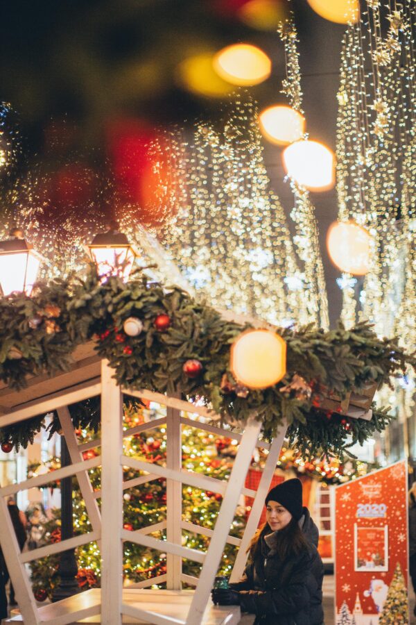 Woman enjoying a Christmas market adorned with festive lights and decorations.